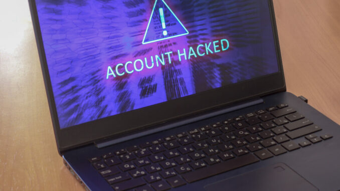 Laptop on the table and on a blue screen the text account is hacked. Warning triangular sign with exclamation mark symbol. Horizontal.