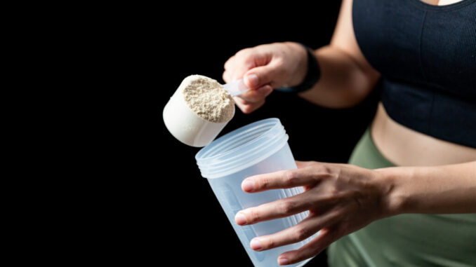 Close up of women with measuring scoop of whey protein and shake